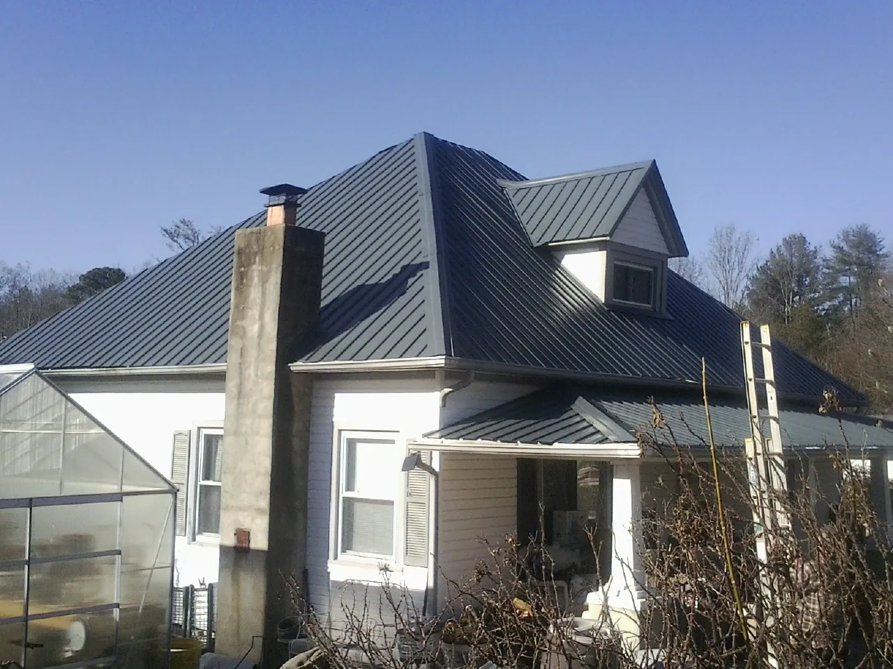 Dark blue standing seam metal roof on a white farmhouse with dormer — Slate & Tile Roof Repair by Roofing Brothers in Hoyt