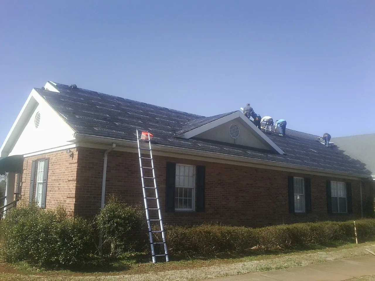 Crew tearing shingles off a brick ranch roof with a ladder set — Emergency Roof Repair work by our crew in Hoyt