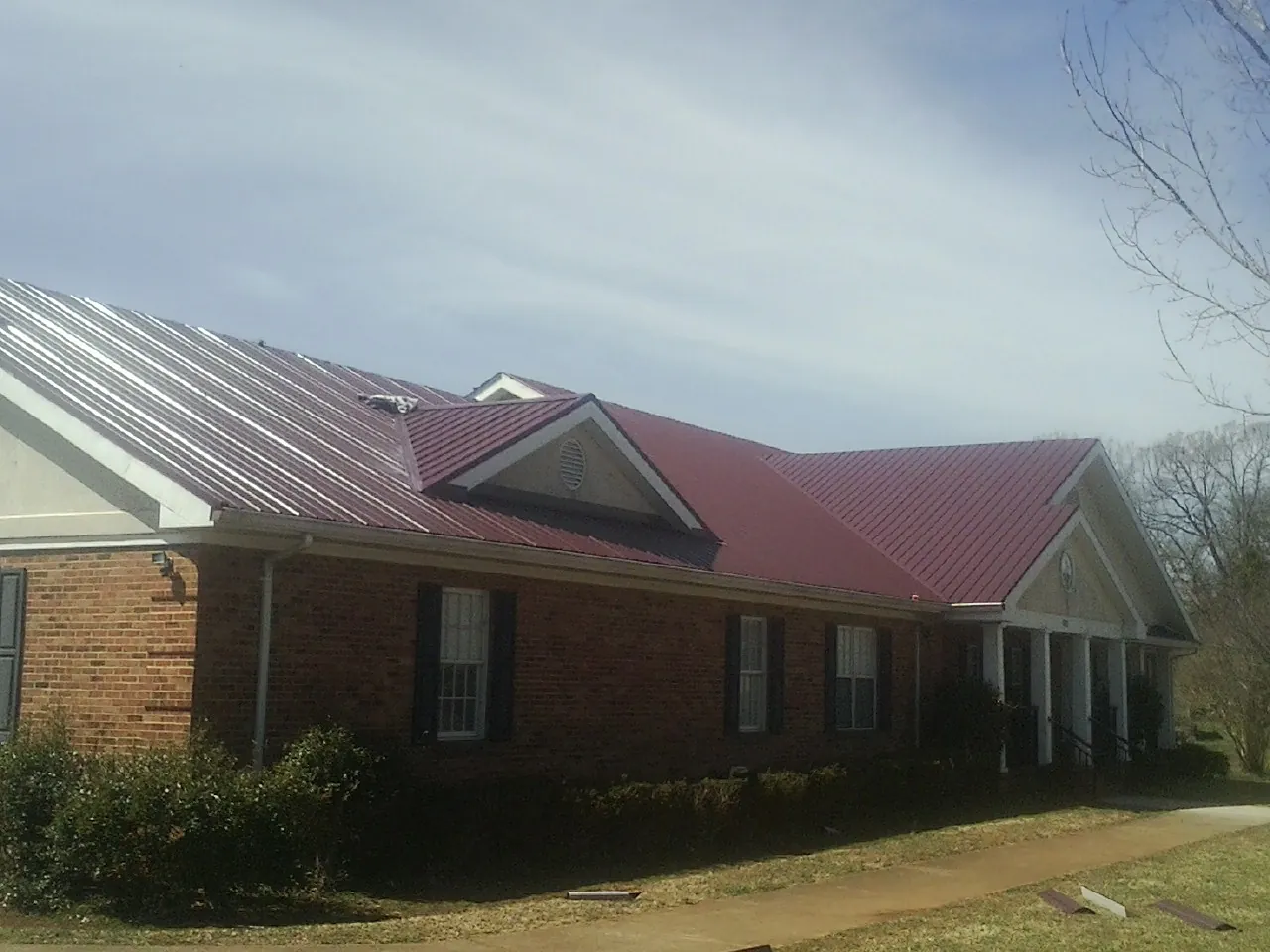 Red metal roof with gabled entries on a long brick building, from a Hail Damage Roof Repair job in Hoyt