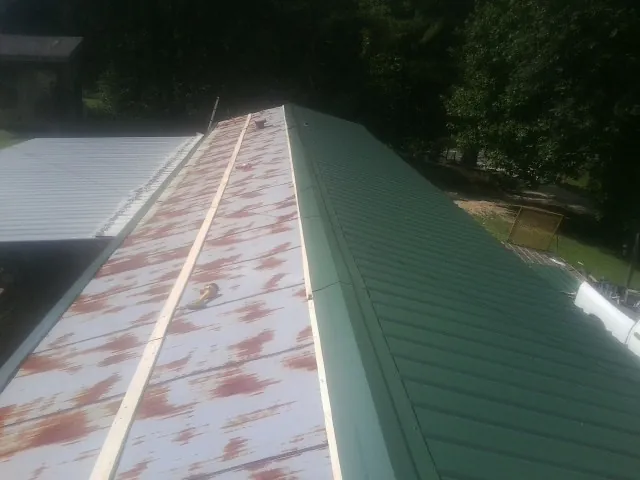Old rusted panels beside newly installed green metal roofing — Wind Damage Roof Repair by Roofing Brothers in Hoyt