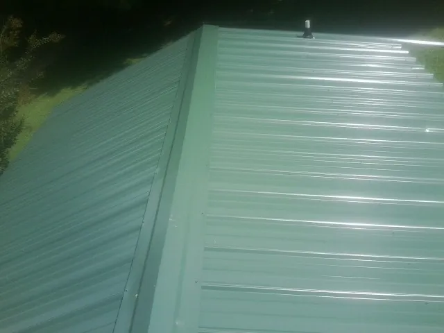 New green metal panels meeting at the ridge of a roof — Flat Roof Repair work by our crew in Hoyt