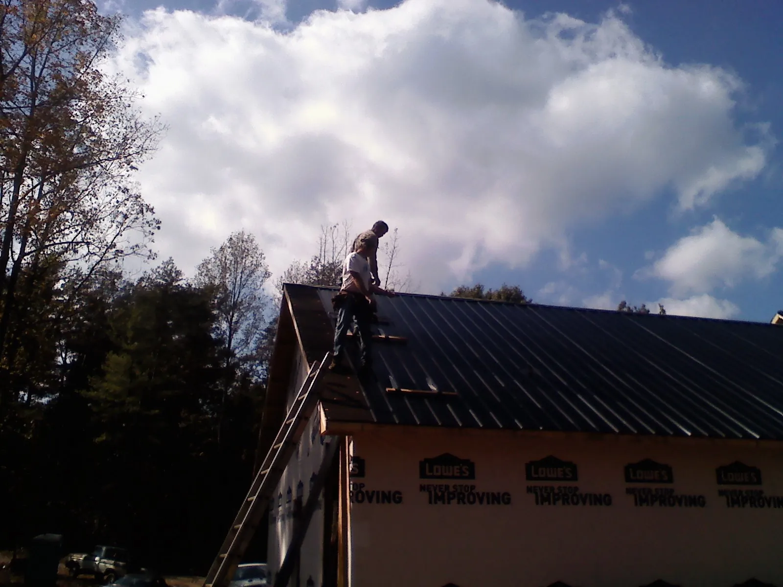 Roofer fastening dark metal panels high against a cloudy sky, from a Roof Inspection job in Hoyt