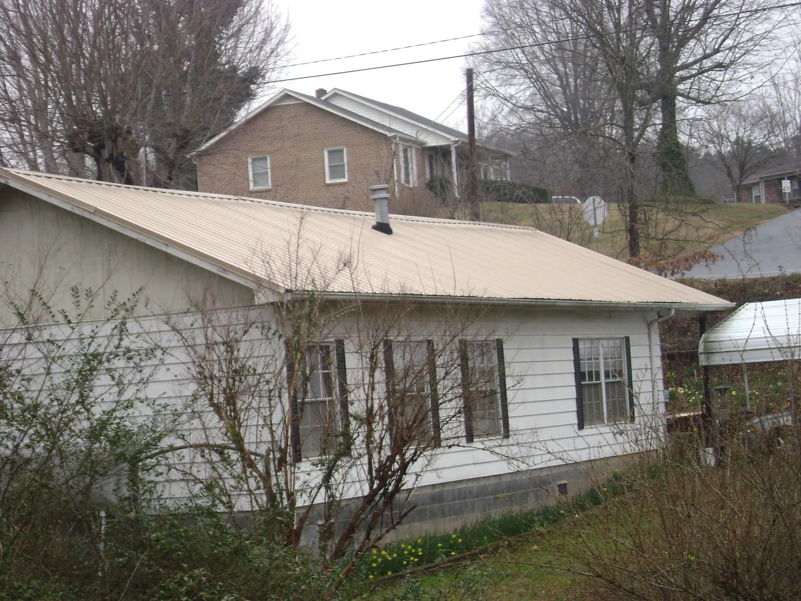 Tan metal roof on a white sided house set into a hillside — Commercial Roofing by Roofing Brothers in Hoyt